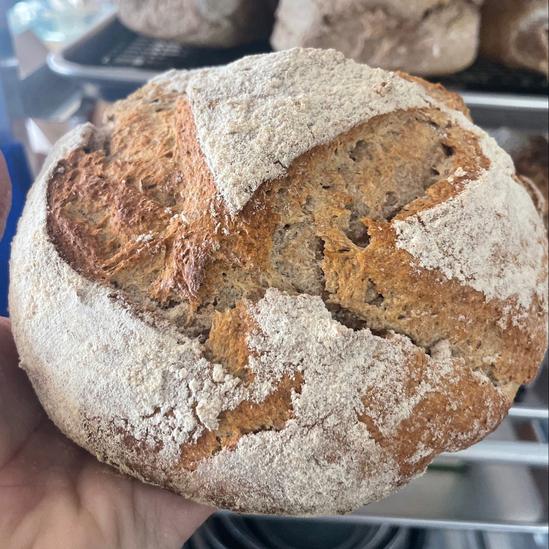 Hand holding a piece of artisan bread with a blurred background of more bread loaves.