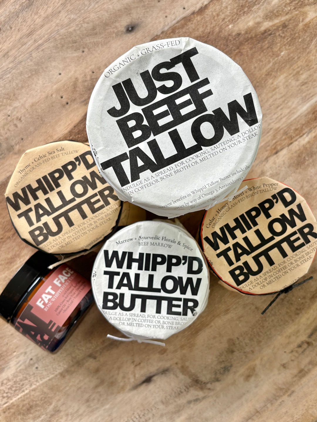 Collection of grass fed beef tallow products including jars and containers on a wooden surface.